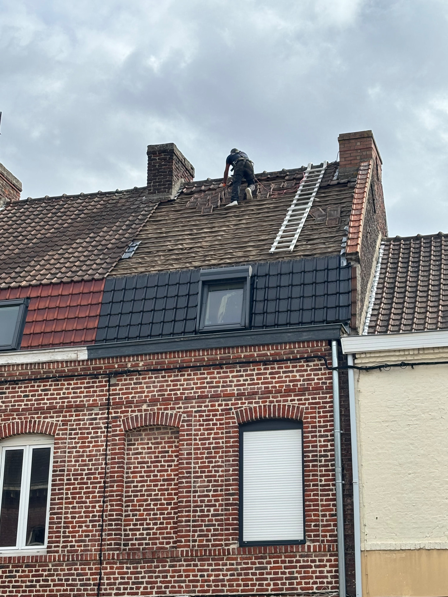Couvreur HS Toiture travaillant sur le faîtage d'une toiture en tuiles